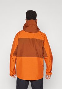Wasserdichte Jacke in leuchtendem Orange mit einem braunen horizontalen Einsatz, Kapuze und langen Ärmeln. Glatte Textur mit verstellbaren Bündchen.