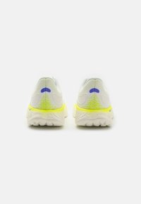 Zapatillas deportivas blancas y amarillas con suelas texturizadas mostradas desde atrás, con detalles en azul y verde neón en el talón.