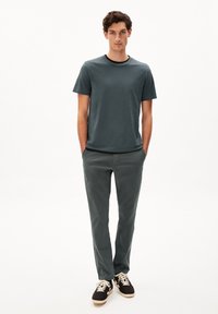 Donkerblauwe crewneck t-shirt, gecombineerd met slim-fit donkergrijze broek. Model draagt zwarte sneakers met beige accenten. Eenvoudig, casual ontwerp.