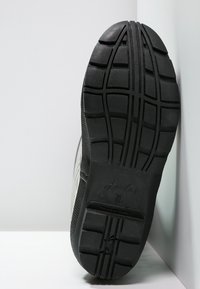 Suola di scarpa in gomma nera con un motivo di battistrada testurizzato, dettaglio del logo e lati rigati verticalmente per una maggiore aderenza e durata.