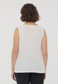 Canotta bianca senza maniche realizzata in un tessuto leggero e morbido. Presenta un ampio scollo arrotondato e un orlo sottile. Design semplice e minimalista.