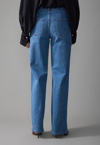 Lys blå, høy midje jeans med rett ben-silhuett. Har to baklommer og en ren hem med lett falming.