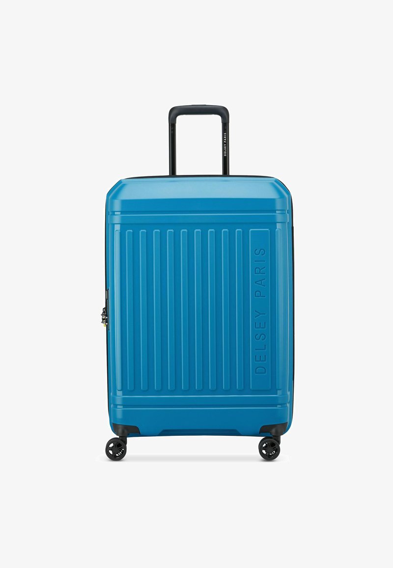 Valise rigide de couleur bleue brillante avec une texture à rainures verticales. Elle est équipée d'une poignée télescopique et de quatre roues noires pour la mobilité.