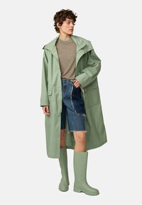 Light green waterproof jacket with a hood, worn over a beige shirt and denim shorts. Paired with matching light green rubber boots.