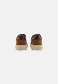 Braune Wildledersneaker mit dunklen Lederakzenten und einer cremefarbenen Gummisohle. Verfügt über eine strukturierte Ferse und ein dezentes Branding-Detail.