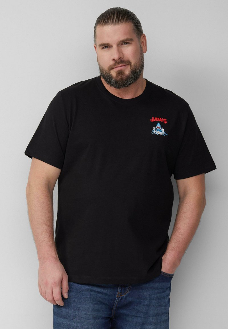 Schwarzes Baumwoll-T-Shirt mit rotem "JAWS"-Logo und buntem Haifisch- und Wellenmotiv; kurzärmliges Design mit Rundhalsausschnitt.