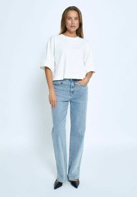Camiseta blanca cortada con mangas cortas, combinada con unos vaqueros de pierna ancha de talle alto en azul claro. Unos tacones negros de punta afilada completan el atuendo.