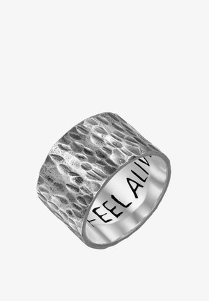 Large bague en argent avec une surface martelée texturée et l'inscription "FEEL ALIVE" gravée à l'intérieur de l'anneau en lettres noires épaisses.