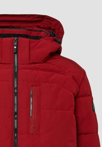 Czerwona puchowa kurtka z wysokim kołnierzem, zamkiem błyskawicznym i kapturem. Posiada pionową kieszeń zapinaną na zamek oraz teksturowane detale na tkaninie.