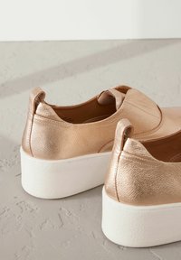 Baskets métalliques rose gold avec une finition texturée, style slip-on, et semelle plateforme blanche ; dotées de languettes arrière pour un enfilage facile.
