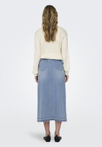Pull en laine crème avec motif texturé, assorti d'une jupe en denim bleu clair, longue, avec un ourlet effiloché et deux poches arrière.
