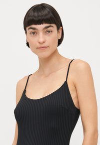 Black ribbed tank top with thin shoulder straps. The fabric has a textured surface, highlighting vertical lines throughout the design.