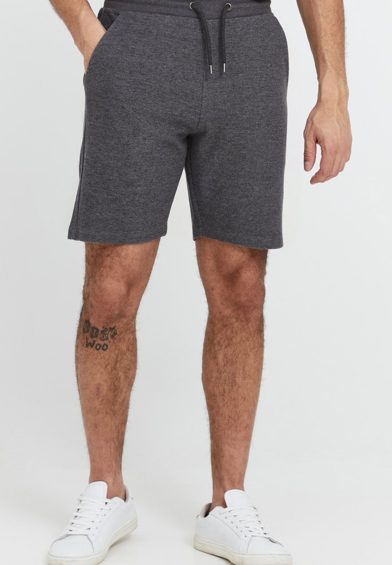 Graue Baumwollmischung-Shorts mit elastischem Bund und Kordelzug, ausgestattet mit Seitentaschen und geradem Schnitt. Getragen mit weißen Turnschuhen.