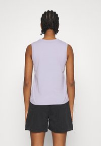 Laventelinvärinen hihaton paita pyöreällä pääntiellä, sileällä pinnalla ja kaarevalla helmalla; yhdistetty mustiin shortseihin.