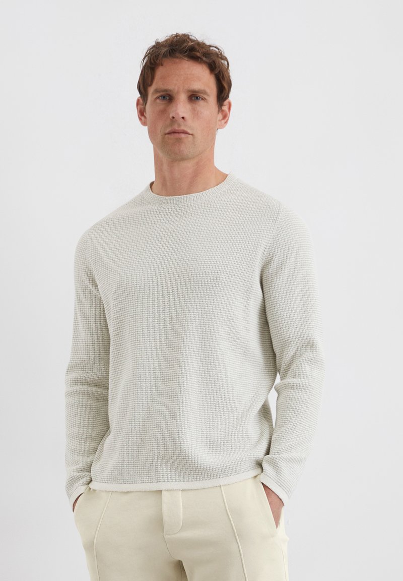 Lichtgrijze, gestructureerde pullover trui met lange mouwen, ronde halslijn en geribbelde zoom, gecombineerd met lichtbeige broeken.