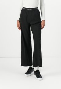 Čierne nohavice s širokými nohavicami a elastickým pásom s logom "Calvin Klein". Hladká látka s uvoľneným strihom a rovnými nohavicami.