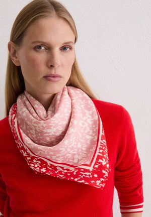 Silk scarf featuring a pink and white floral pattern, edged in red, worn around the neck over a red sweater with ribbed accents.