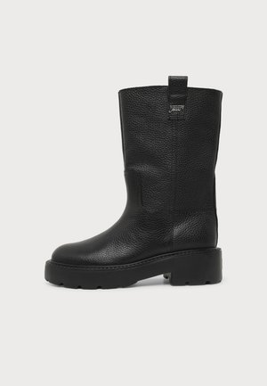 Bottes en cuir noir mi-mollet avec surface texturée, languette de traction en haut et semelle épaisse à crampons pour adhérence et durabilité.