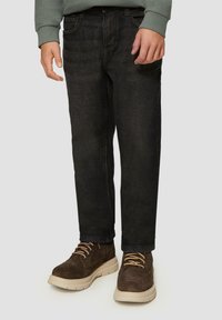 Schwarze Denim-Hosen in Slim-Fit mit fünf Taschen und einer subtilen Textur, kombiniert mit braunen Schnürstiefeln mit dicker Sohle.