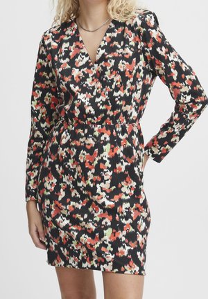 Woman wearing a long-sleeve, V-neck mini dress with a black, red, white, and green abstract floral pattern against a plain background.