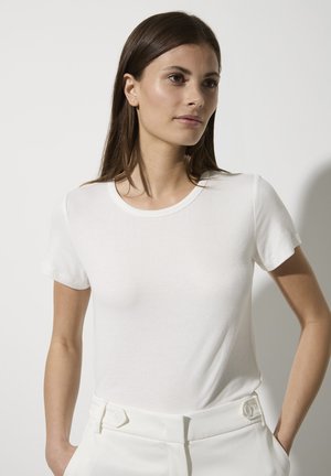 Weißes, geripptes T-Shirt mit kurzen Ärmeln, rundem Ausschnitt und weichem Material. Kombiniert mit weißen, hochtaillierten Hosen mit Knopfdetails.
