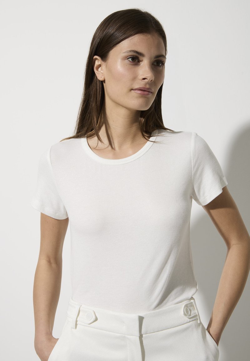 Weißes, geripptes T-Shirt mit kurzen Ärmeln, rundem Ausschnitt und weichem Material. Kombiniert mit weißen, hochtaillierten Hosen mit Knopfdetails.