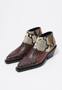 Botas de tobillo de piel de serpiente con punta afilada, en tonos mezclados de marrón, negro y beige, con un acabado texturizado y un tacón bajo en forma de cuña.