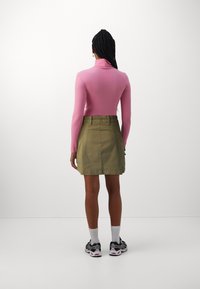 En figurnära rosa långärmad topp i kombination med en khakifärgad kjol. Toppen har hög hals och kjolen har en platt midjeband och sidofickor.