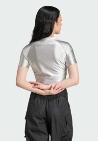 Silverkort topp med korta ärmar, med en slät, glänsande textur. I kombination med svarta cargo byxor som har en avslappnad passform.