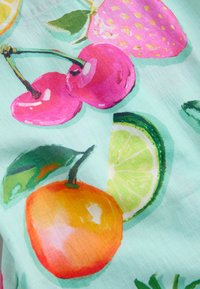 Világos színű szövet festett cseresznyékkel, egy rózsaszín eperrel, egy narancssárga gyümölccsel egy levéllel és egy lime gerezddel világoskék háttéren.