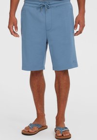 Shorts en sweat bleu clair en matière douce, avec une taille à cordon de serrage ajustable, des poches latérales et des détails de logo brodés.