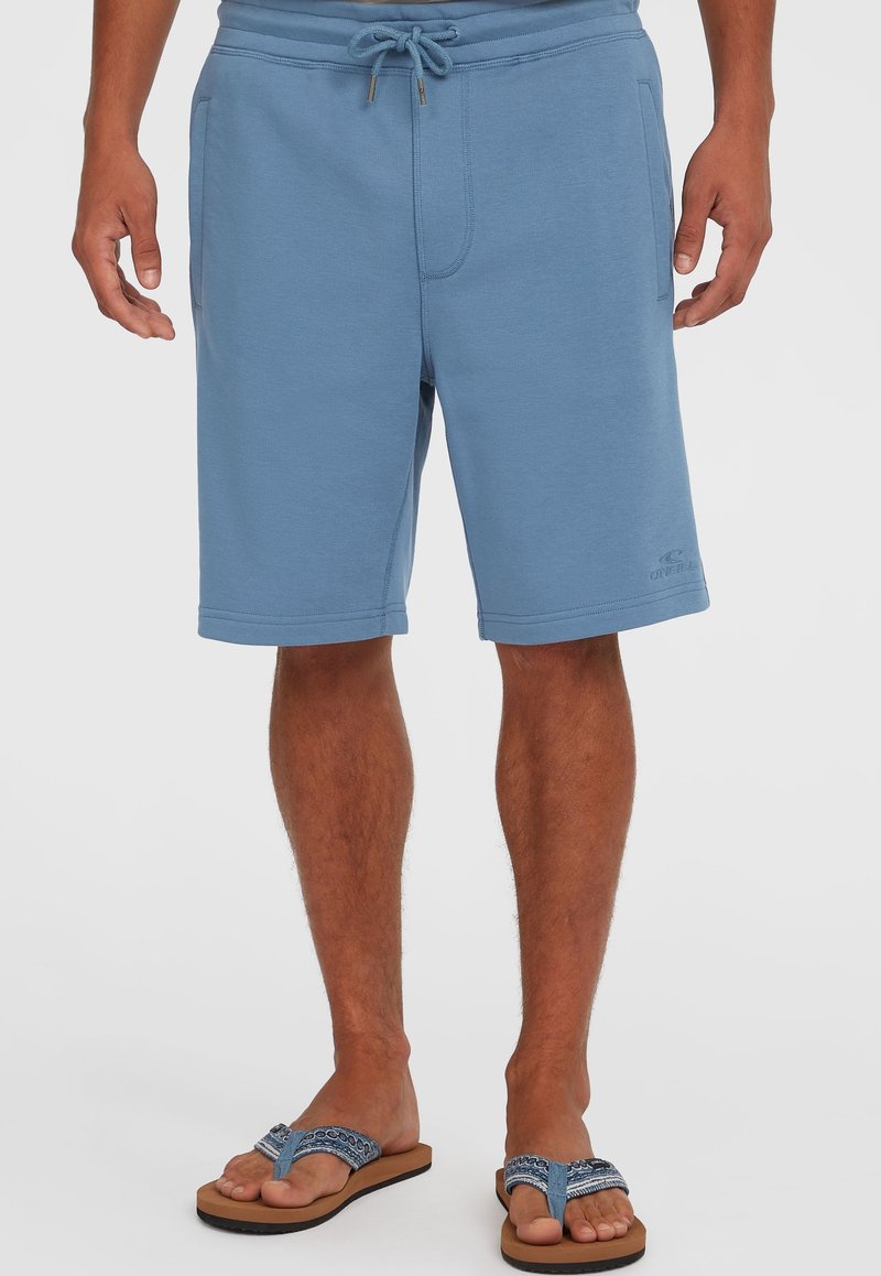 Shorts en sweat bleu clair en matière douce, avec une taille à cordon de serrage ajustable, des poches latérales et des détails de logo brodés.