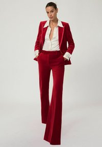 Röd sammetsdräkt med en åtsittande blazer och vida byxor. Vit skjorta under. Slen yta, skräddarsydd passform och en polerad look.