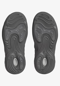 Zwarte sneakerzolen met complexe golvende patronen, textuur rubber oppervlakken en een ronde zilveren accent op het hielgebied.