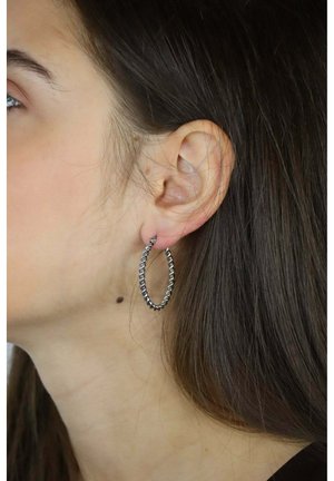 Orecchino a cerchio torsionato in argento, leggero, con finitura lucida e forma ovale leggermente irregolare, sospeso da un piccolo fermaglio.