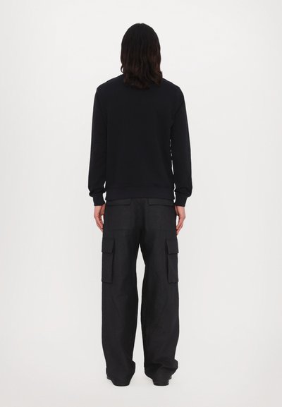 Zwarte sweatshirt met lange mouwen en geribde manchetten, gecombineerd met losse zwarte cargobroek met meerdere zakken.