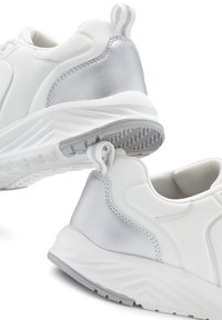 White athletic shoes with a silver accent on the heel. Made of smooth material with a textured sole and a pull tab at the back.