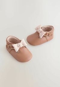 Leather baby shoes in soft pink, featuring a rounded toe, strap with gold buckle, and a bow accent on the front. Smooth texture.