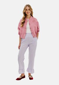 Ružová vyšívaná bunda, biela tričko a levandulové kárované nohavice s volánmi na lemoch. Červené baleríny so strapcovým detailom dokončujú outfit.