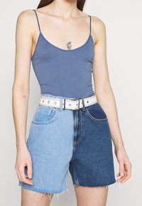 Niebieski prążkowany top na ramiączkach zestawiony z kolorowymi szortami dżinsowymi, które mają jasnoniebieską i ciemnoniebieską część oraz białym paskiem.