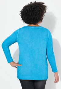 Langärmliges blaues Oberteil aus weichem Stoff, mit runder Ausschnitt, seitlichen Schlitzen und einer lockeren Passform im Rücken.