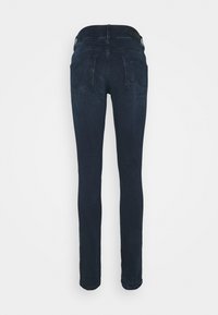 Jean slim bleu foncé vu de dos, avec deux poches arrière et passants pour ceinture à la taille.