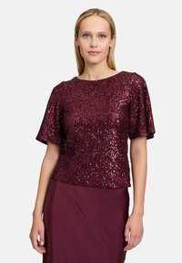 Top di paillettes borgogna con maniche corte, caratterizzato da un collo rotondo e una superficie texture. Indossato con una gonna abbinata.
