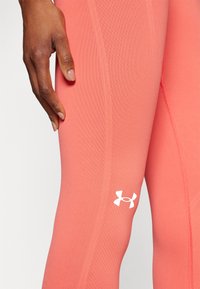 Korall színű sportleggingsz, textúrált anyaggal és testhezálló szabással. Az alsó lábszáron egy kis fehér Under Armour logó található.