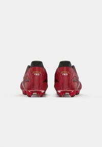 Sarkani futbola zābaki ar elegantu dizainu, ar melnu apkakli, strukturētām virsmām un sarkaniem spikes. Uz papēža redzams zīmola nosaukums "Morelia Neo."