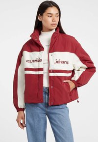Rød og hvid farveblok jakke med logoerne "GUESS" og "Jeans," elastiske manchetter, høj krave og trykknapper fortil.