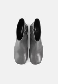 Botas de tobillo de cuero gris con una silueta elegante, acabado suave y detalles de costura sutiles; cremalleras en los lados y plantillas con marca.