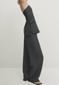 Combinaison noire sans bretelles, à jambes larges et à coupe ample, avec un tissu texturé et des fentes sur les côtés pour un détail supplémentaire.