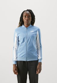 Svetlomodrá zipsová bunda s bielymi akcentmi, vyrobená z hladkej tkaniny. Má stojatý golier a ribované manžety. Logo je umiestnené na hrudi.