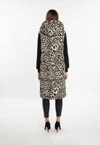 Bézs színű, fekete leopárdmintás, párnázott, térd alá érő mellény, nagy kapucnival és oldalsó zsebekkel, fekete leggings-szel és magassarkú cipővel párosítva.